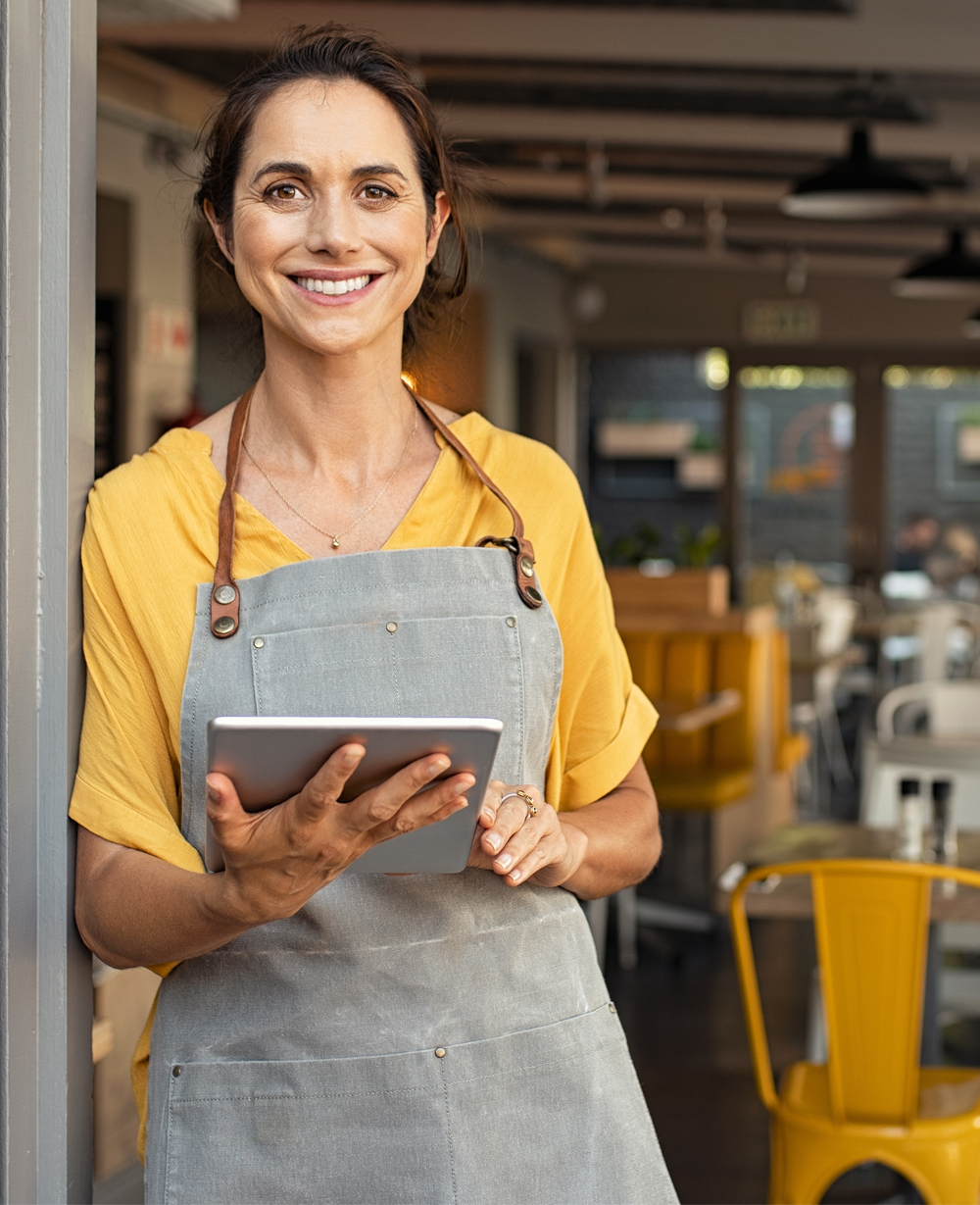 Business owner wearing a yellow apron, standing in front of business.