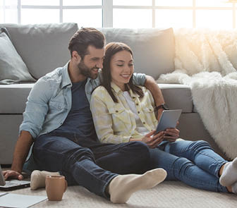 Young couple looking at tablet while sitting on floor in front of a couch